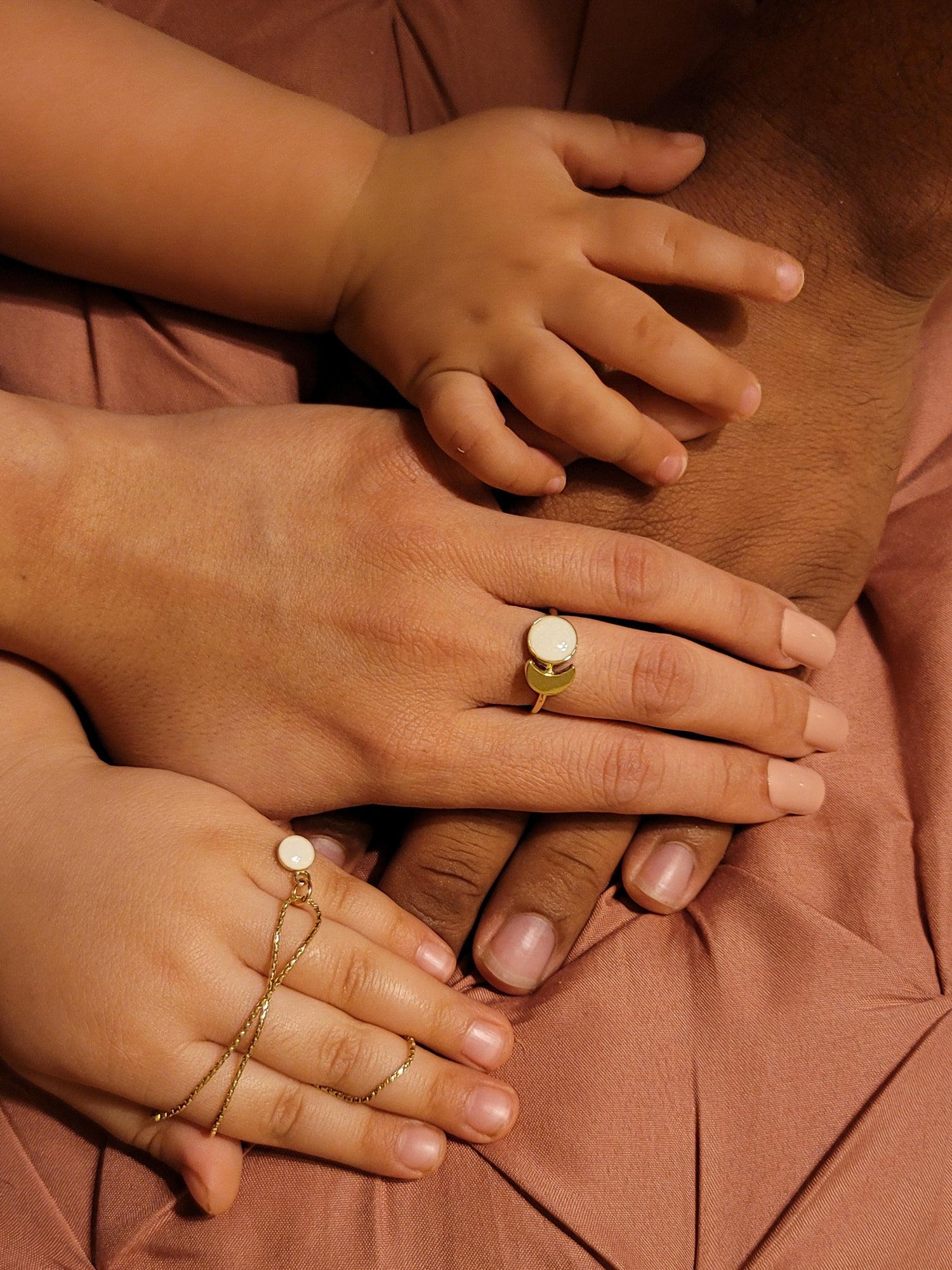 Hands of a mother wearing a breast milk ring and her children holding a breast milk necklace.