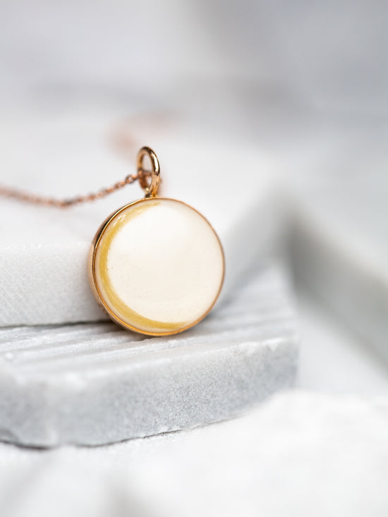 A round breast milk pendant with a lock of blonde hair