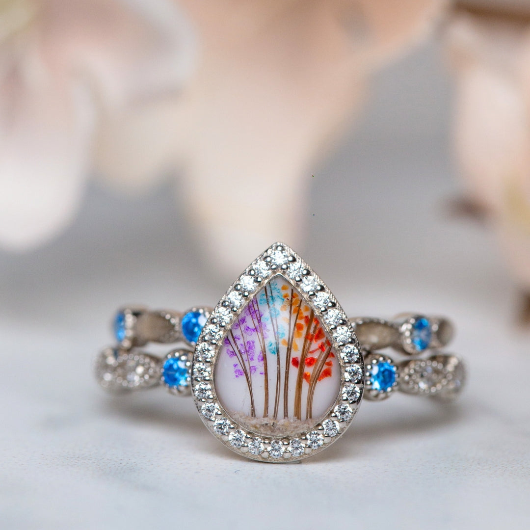 Teardrop-shaped ring with floral design and gemstones on a soft background
