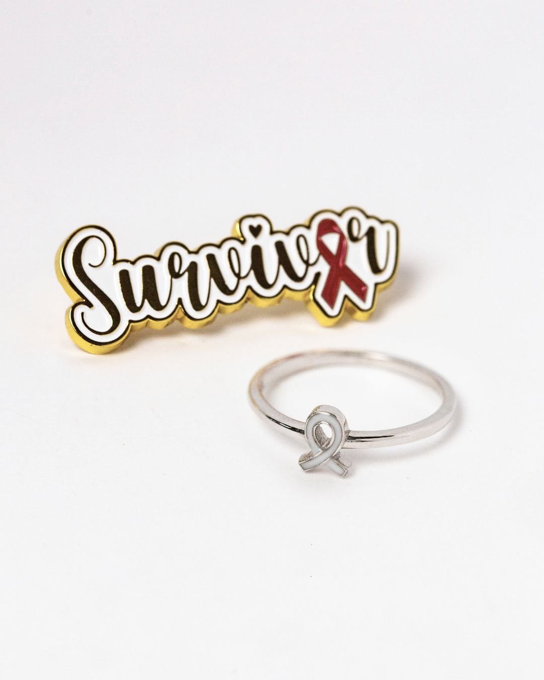 Sterling silver awareness ribbon breastmilk keepsake ring displayed beside survivor badge for breast cancer tribute
