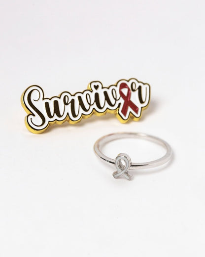 Sterling silver awareness ribbon breastmilk keepsake ring displayed beside survivor badge for breast cancer tribute