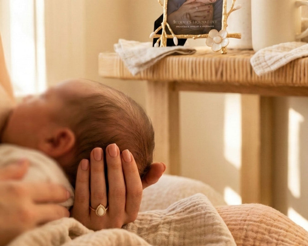Mother holding her newborn beside a bedside table displaying a Mamma’s Liquid Love keepsake picture frame in a warm nursery setting
