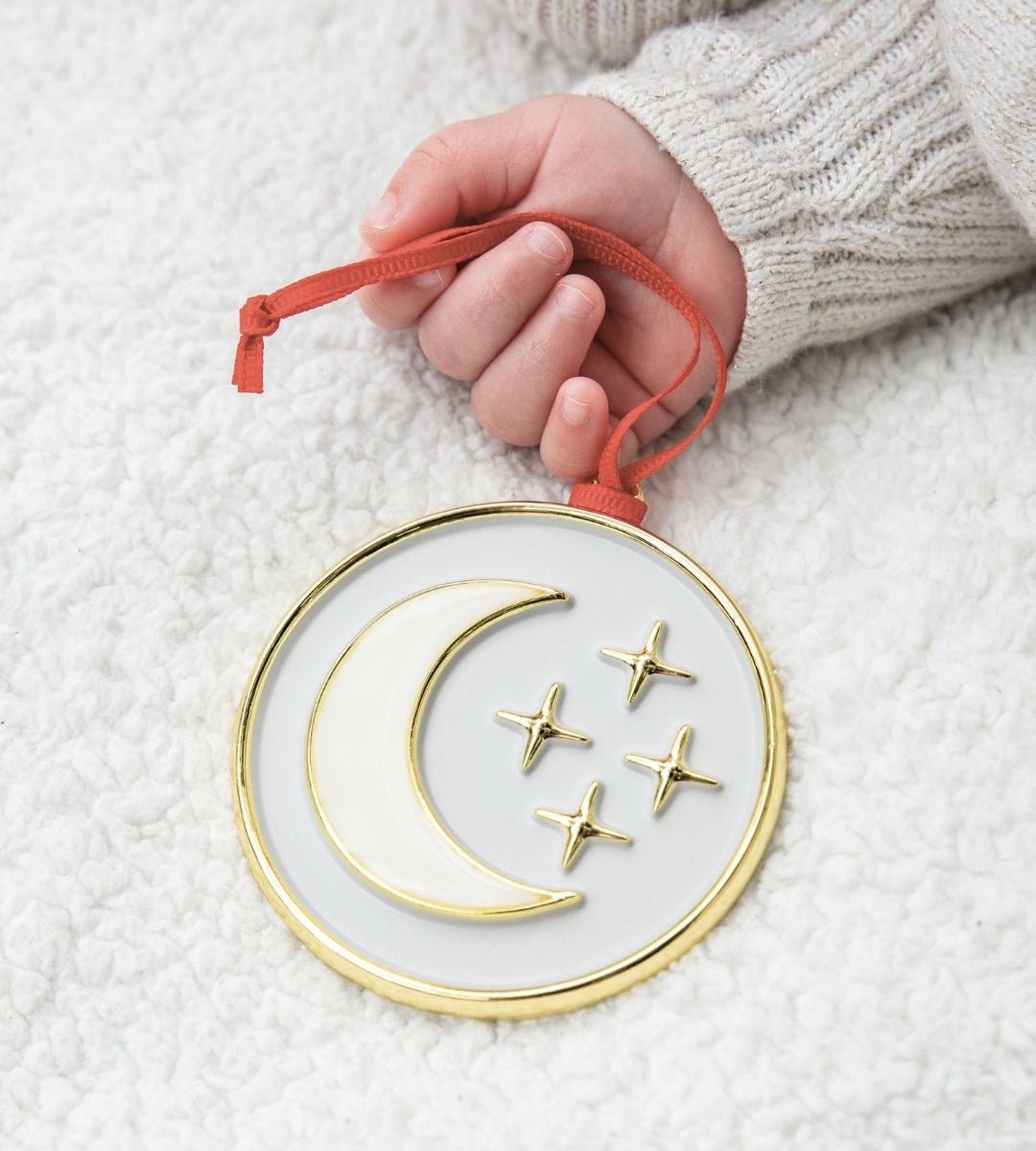 Baby hand holding the My Moon and Stars ornament with gold moon and stars design.