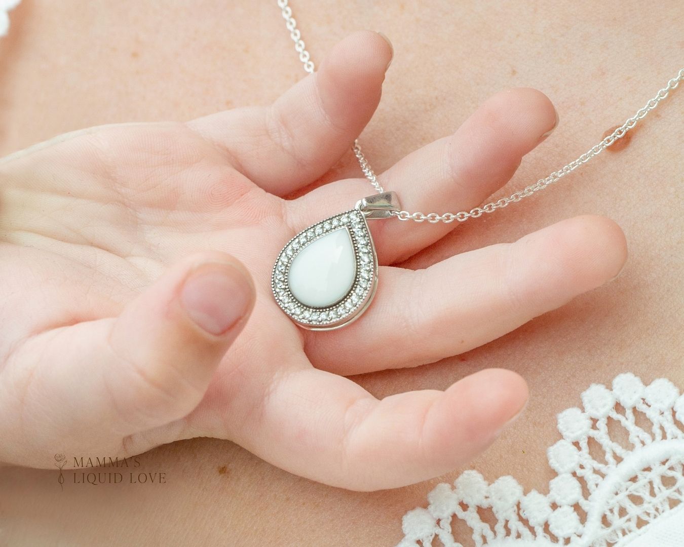 White Gold Love Drop necklace with preserved breastmilk stone held in a mother’s hand