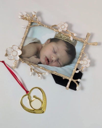 Gold floral frame from Mamma’s Liquid Love with a baby photo beside a gold heart-shaped breastmilk ornament on a red ribbon.
