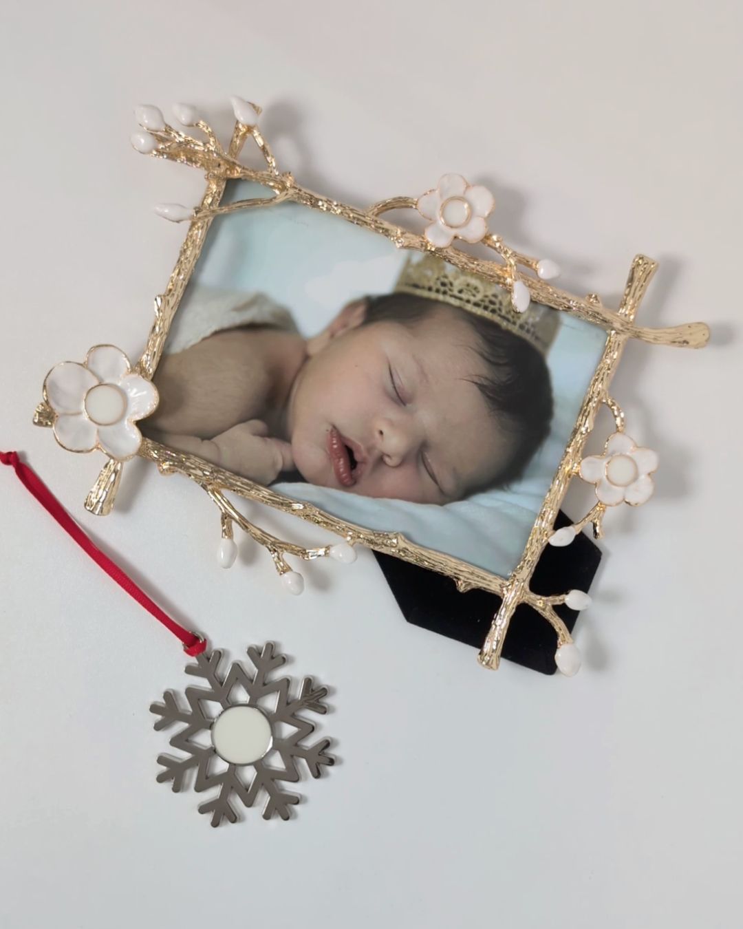 Gold floral frame from Mamma’s Liquid Love with a baby photo beside a silver snowflake-shaped breastmilk ornament on a red ribbon.