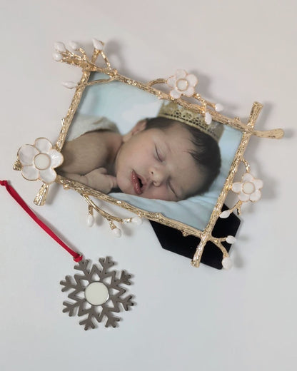 Gold floral frame from Mamma’s Liquid Love with a baby photo beside a silver snowflake-shaped breastmilk ornament on a red ribbon.